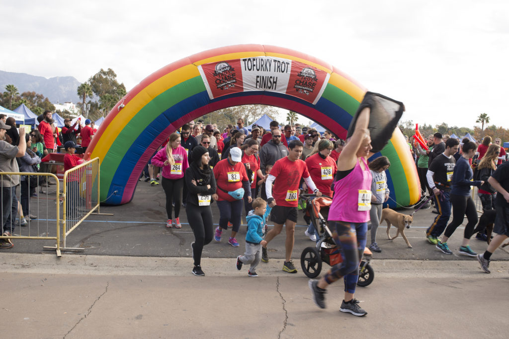 Racers cross the finish line, an inflatable rainbow arch, at a Tofurky Trot